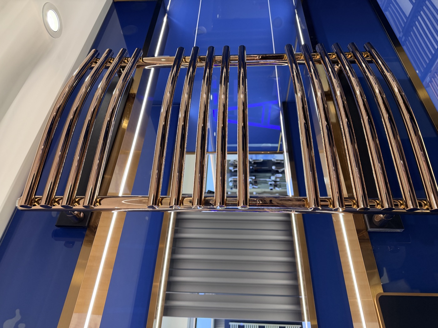 Design-Handtuchheizkörper in Kupfer/Roségold vor blauer Showroom-Wand